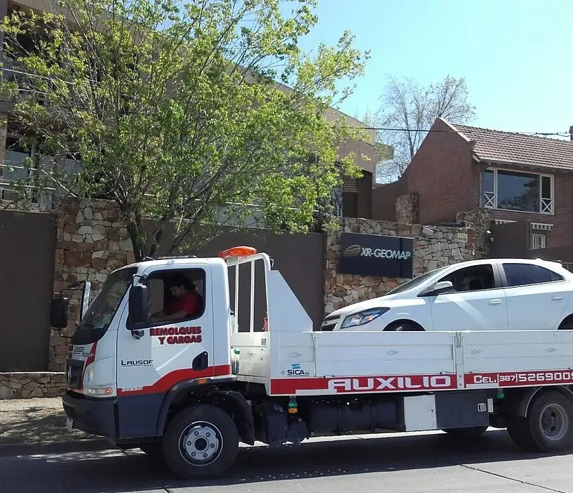 Lausof flatbed tow truck carrying a car through the city of Salta