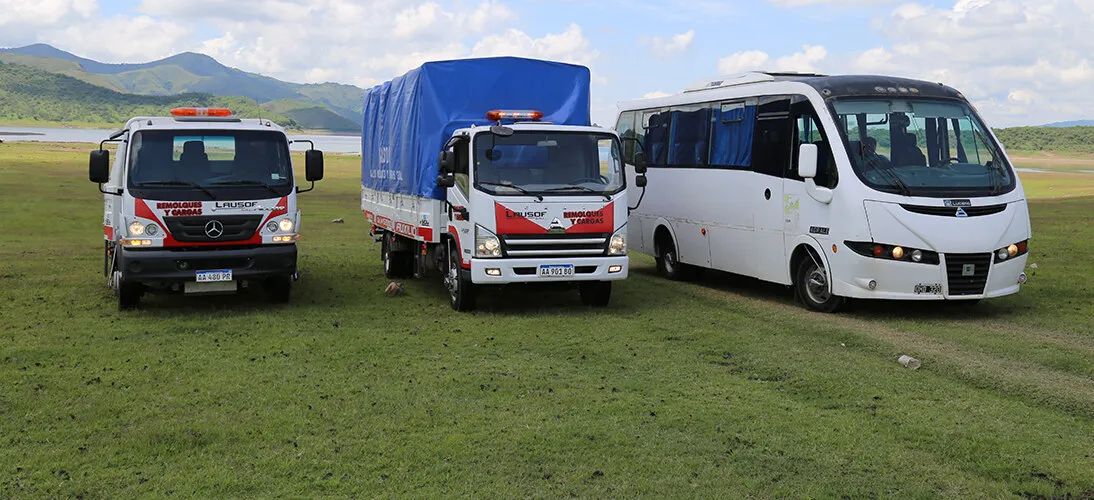 A Lausof tow truck, a curtain-side freight truck and a passenger minibus lined up in front of the hills of Salta